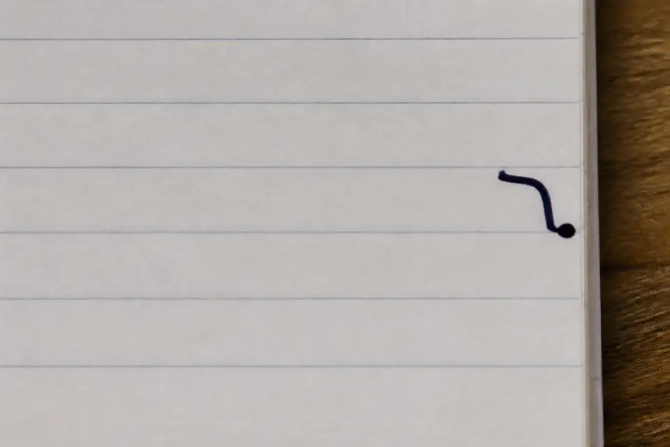 A dark ink dot on the right margin of a lined notebook, where a Hebrew letter is about to begin